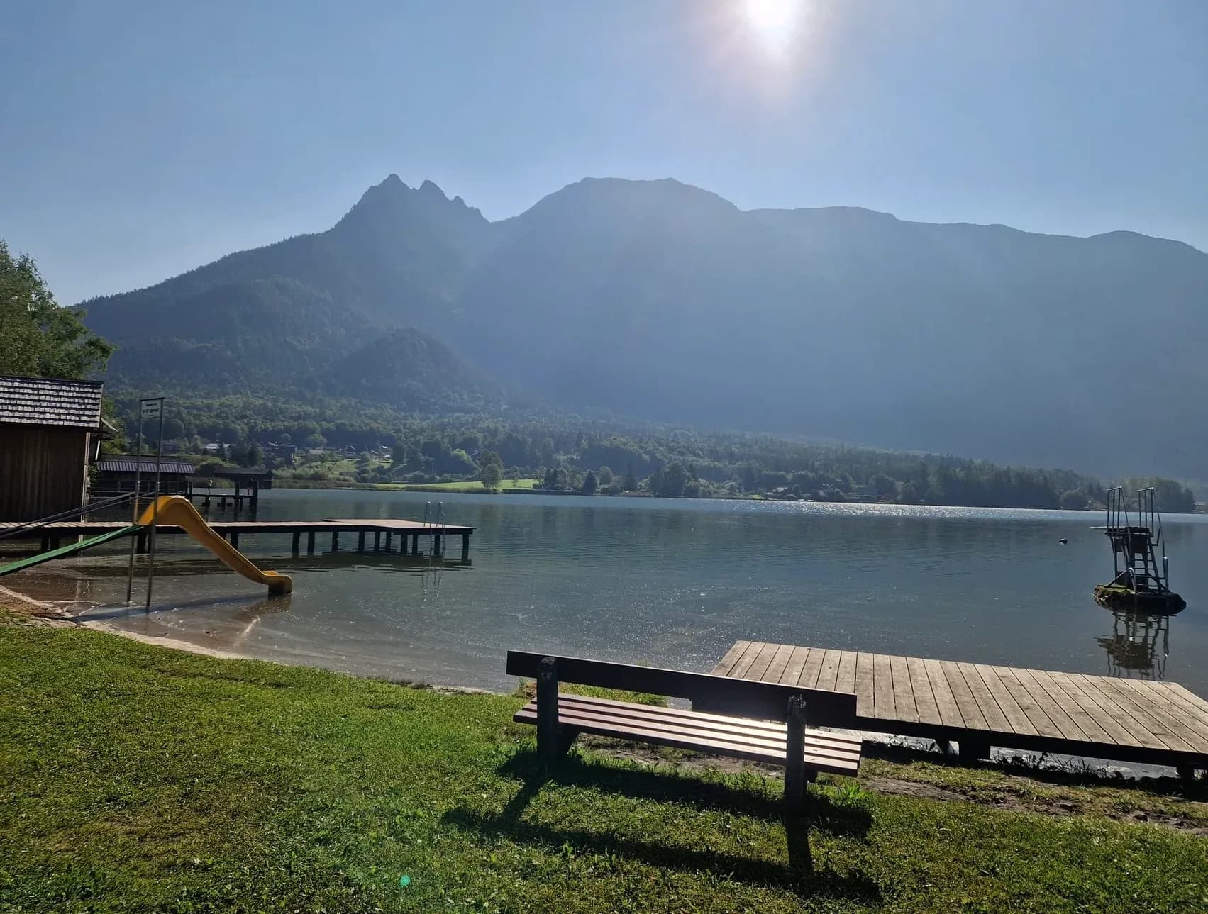 Holzbank und Badesteg an einem Bergsee in der Morgensonne